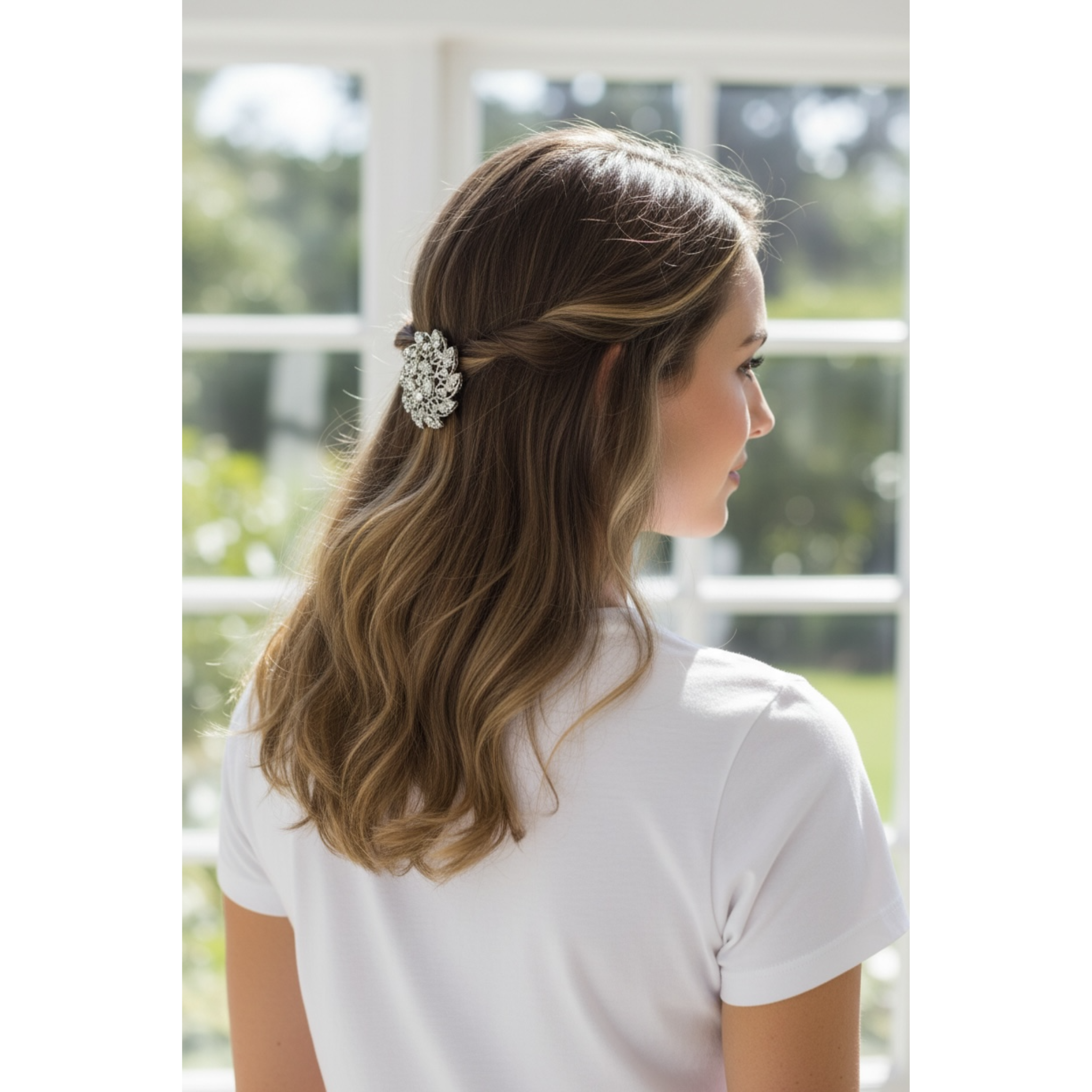 Woman with a decorative hair clip in her hair, standing in front of a window with a view of greenery.