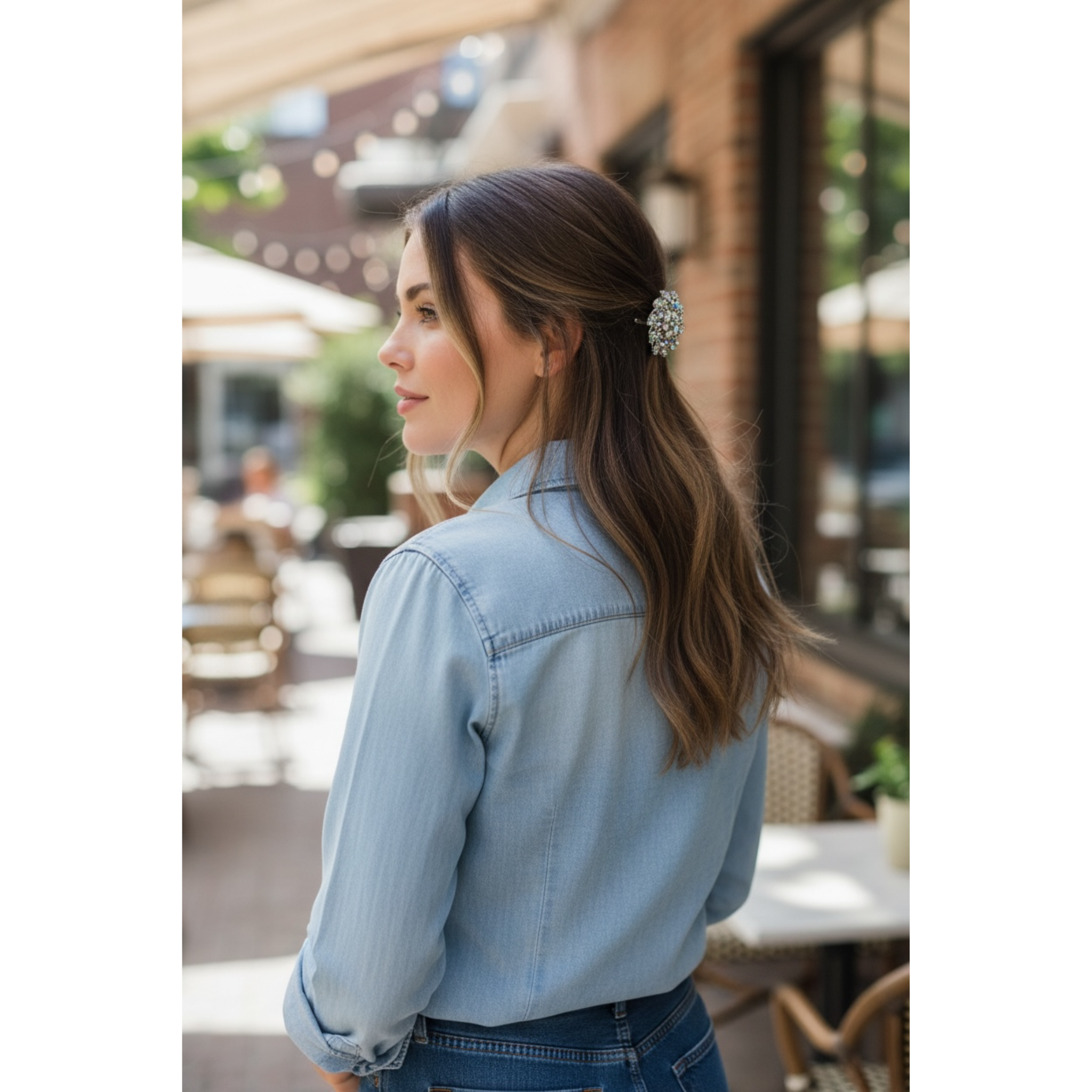 Woman wearing a light blue denim shirt with a blurred outdoor setting. This image highlights the beautiful decorative multicolor hair clip in the woman's styled hair.