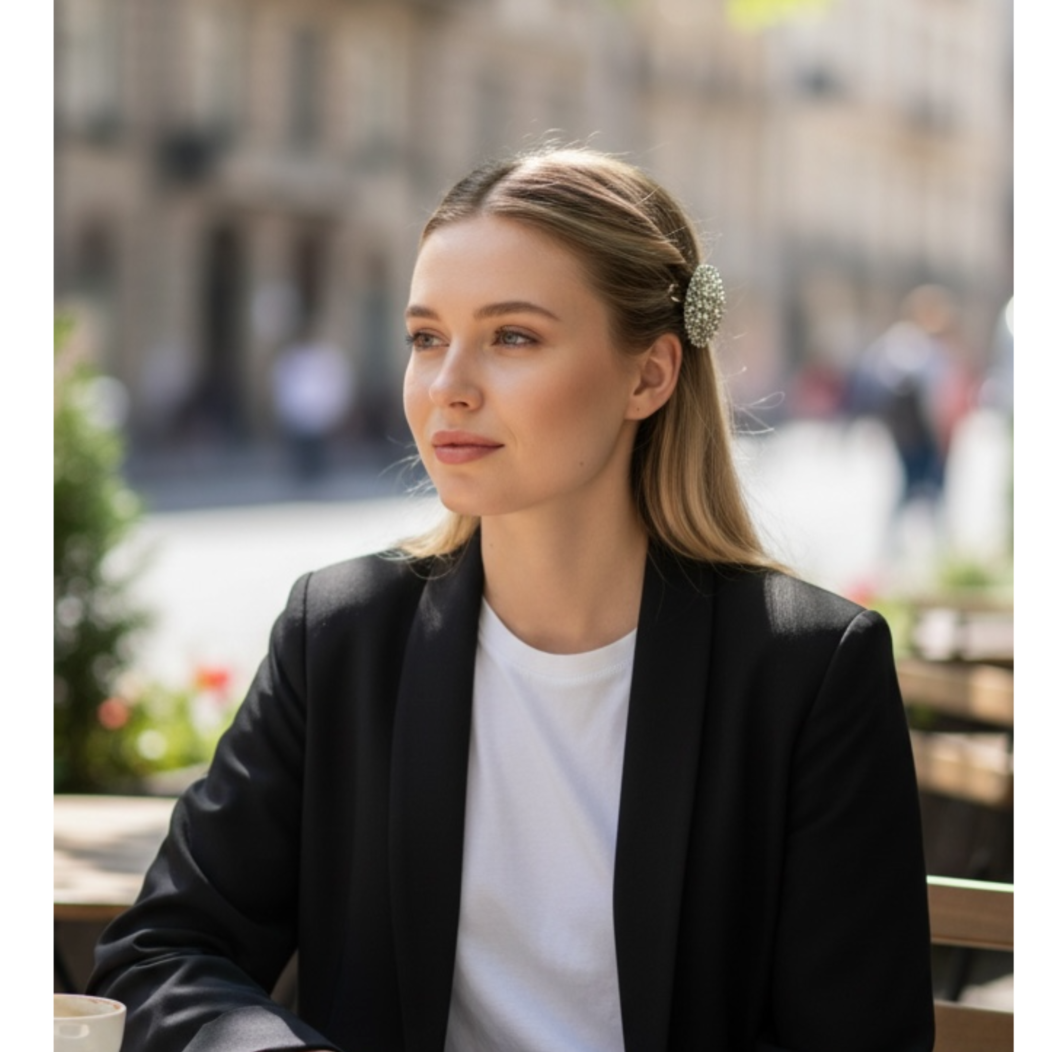 Woman sitting outdoors wearing a black blazer and white shirt, with a blurred background