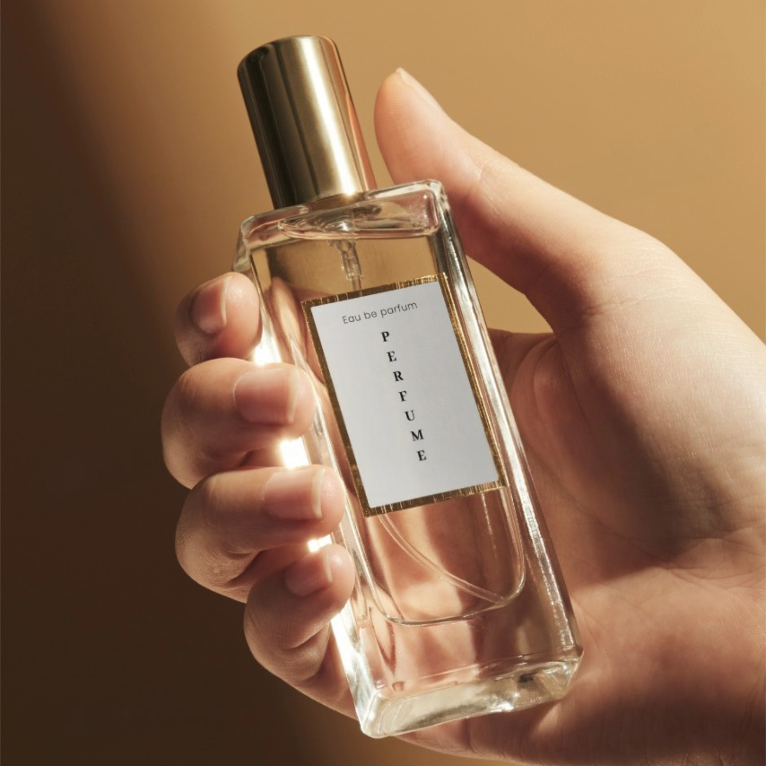 Hand holding a perfume bottle with a gold cap against a warm background.