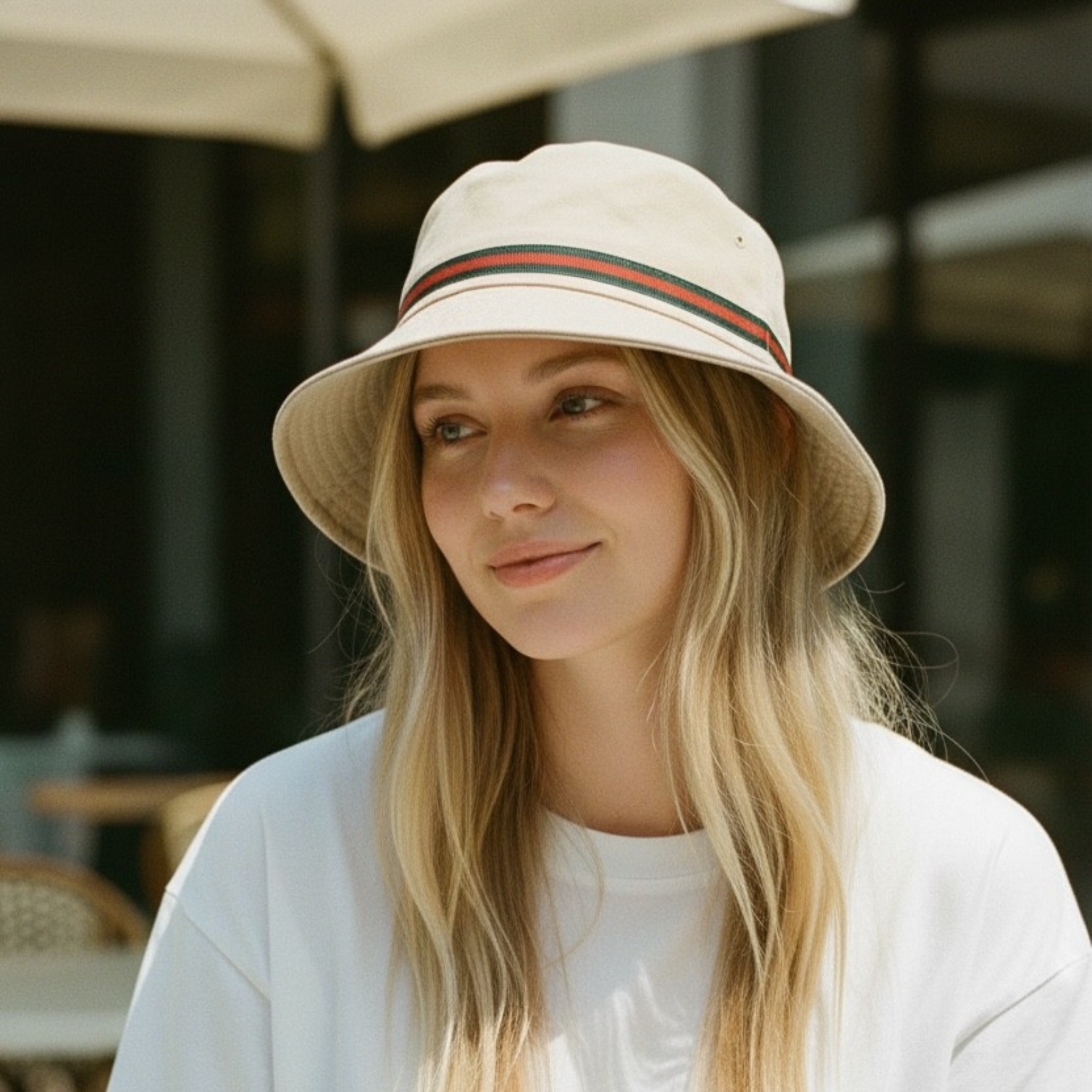 Woman wearing a beige bucket hat with a striped band outdoors. The stripes are green and red.
