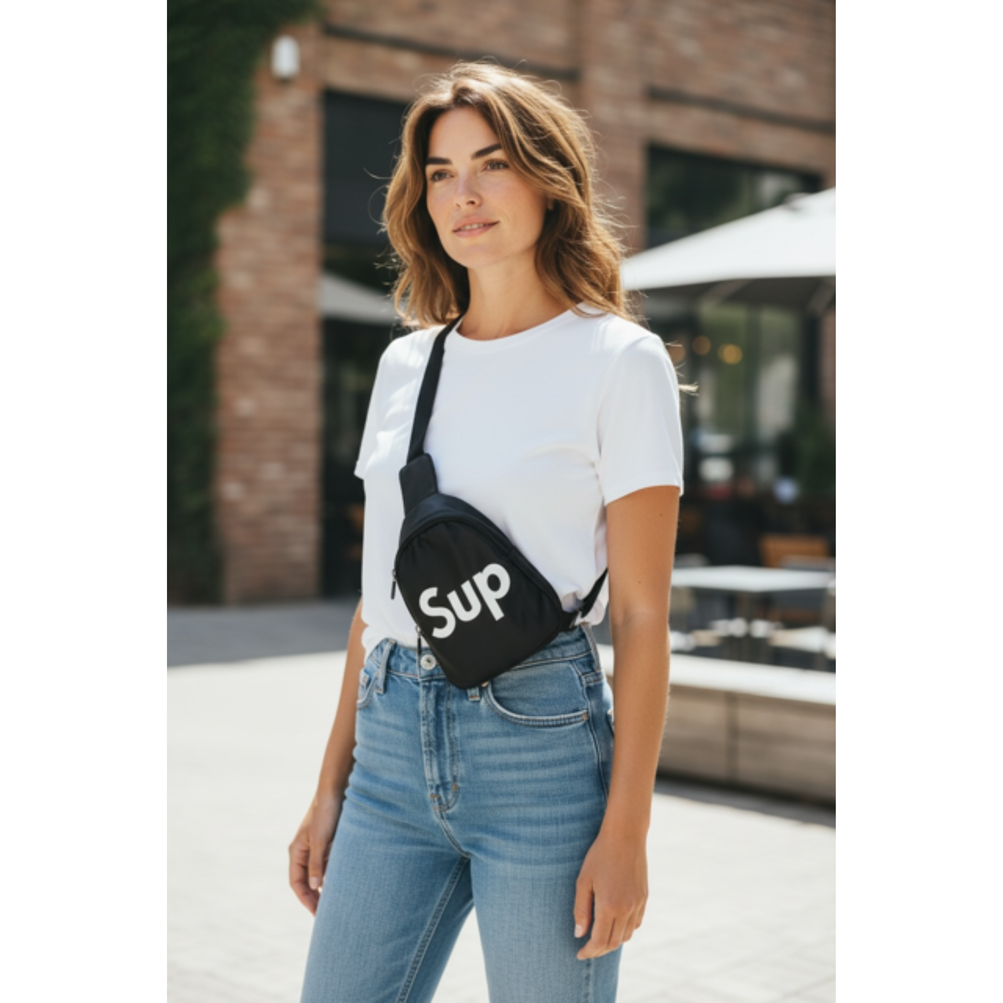 Woman wearing a white t-shirt with 'Sup' logo crossbody bag and blue jeans.
