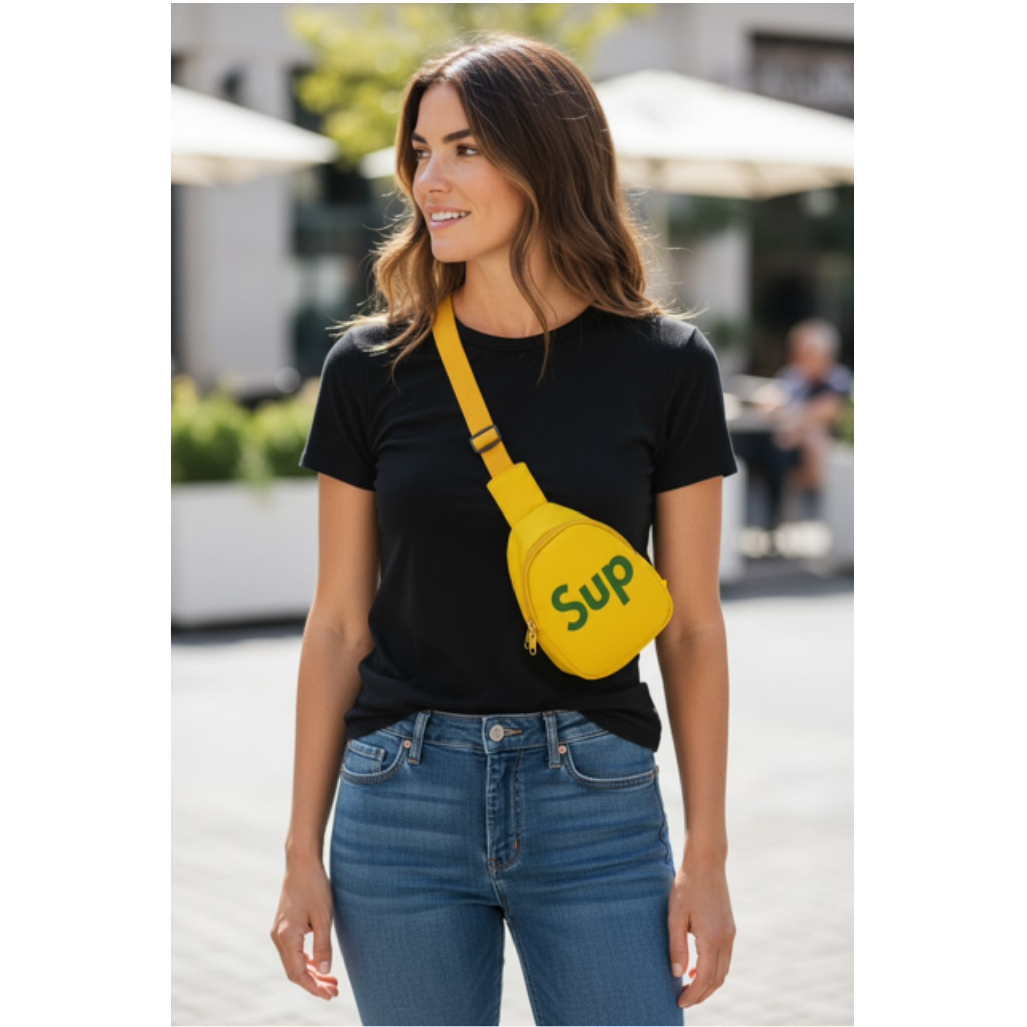 Woman wearing a black t-shirt and blue jeans with a yellow sling bag with the text 'Sup' on it, with a background in the city outdoors.